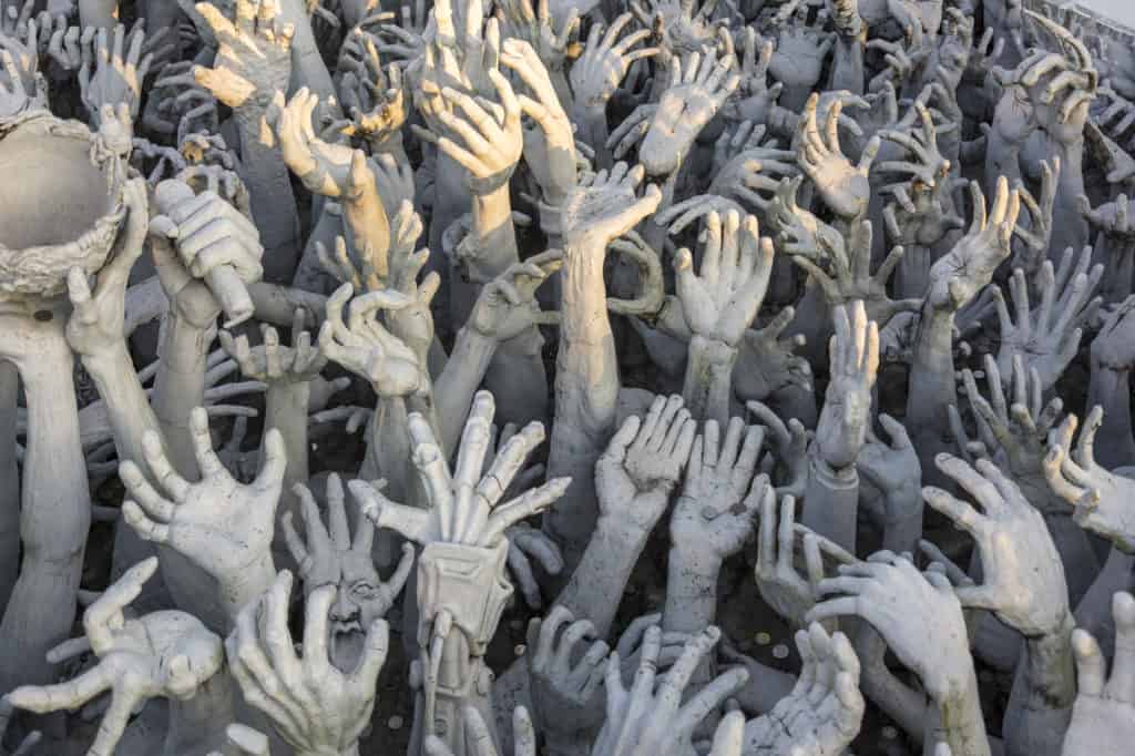 Hände aus Stein strecken sich aus der Hölle im Weißen Tempel von Chiang Rai in die Richtung Himmel