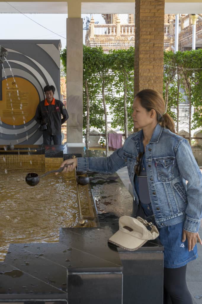 Junge Thailändische Frau fängt das heilige Wasser eines Brunnens auf