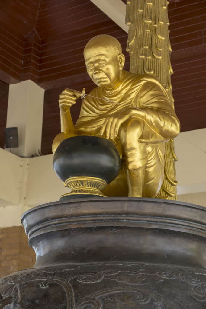 Die Statue des ehrwürdigen Luang Phoo Khoo Prisuddho beobachtet die Szenerie der wassertrinkenden Frau