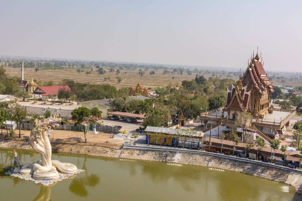 Blick über die Ebene im Isaan mit der Naga Schlange und dem Bot des Wat Ban Rai dem Elefanten-Tempel in Thailand