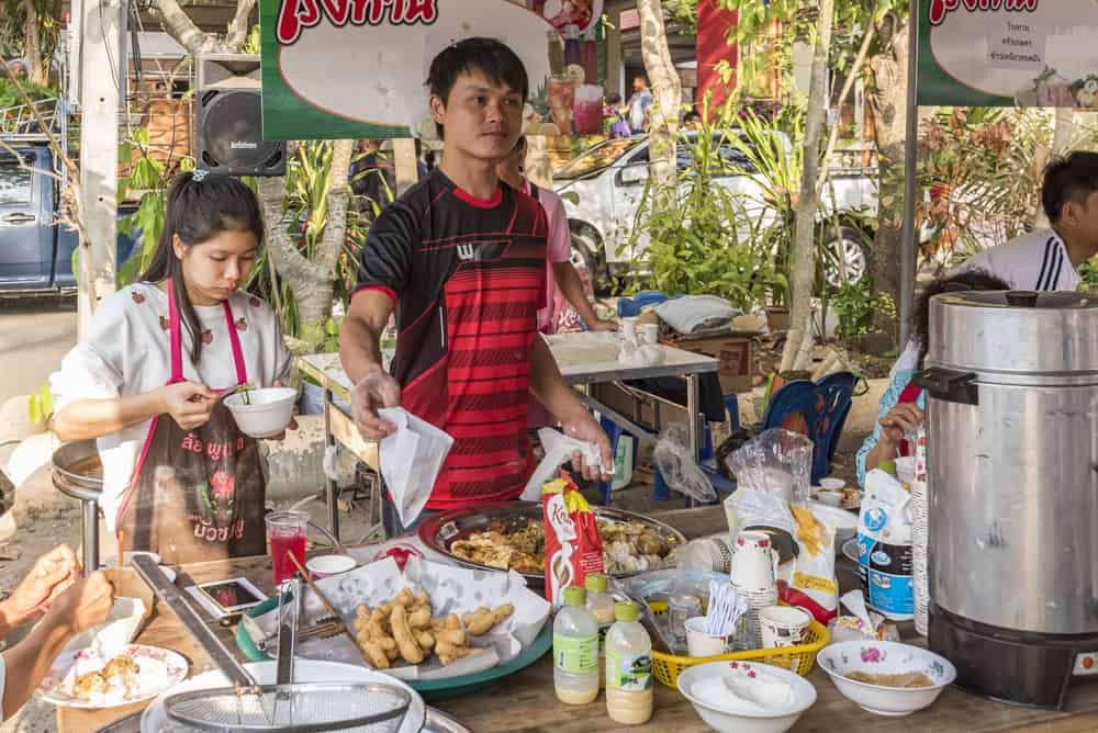 Thailändischer Essenstand bei dem zwei Personen Speisen an die Besucher kostenlos verteilen beim Geburtstag eines Mönches