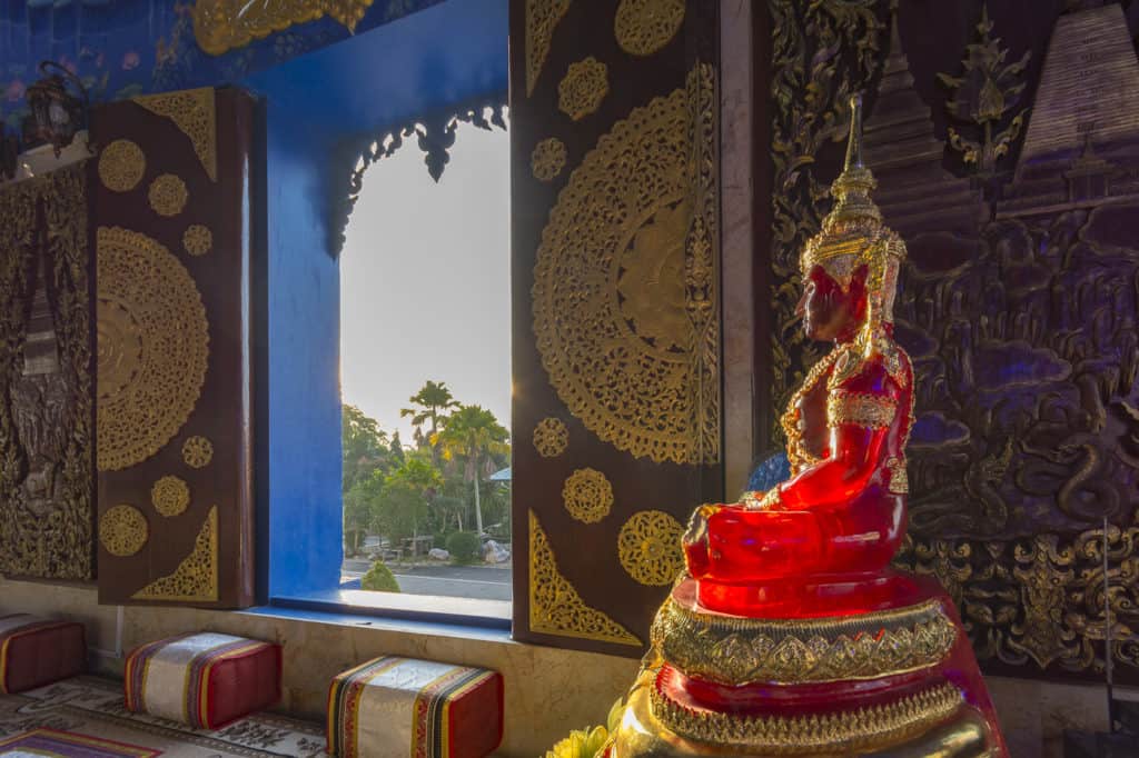 Magisch scheint die rote Buddhafigur in der Morgensonne im Blauen Tempel in Chiang Rai - Nordthailand