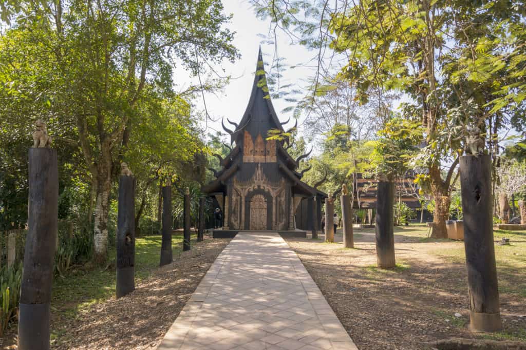 Holzhaus mit Zügen eines Tempels und den Weg gesäumt mit Tierfiguren auf Holzstämmen - Künstler Thawan Duchanee - Schwarze Haus in Chiang Rai - Thailand