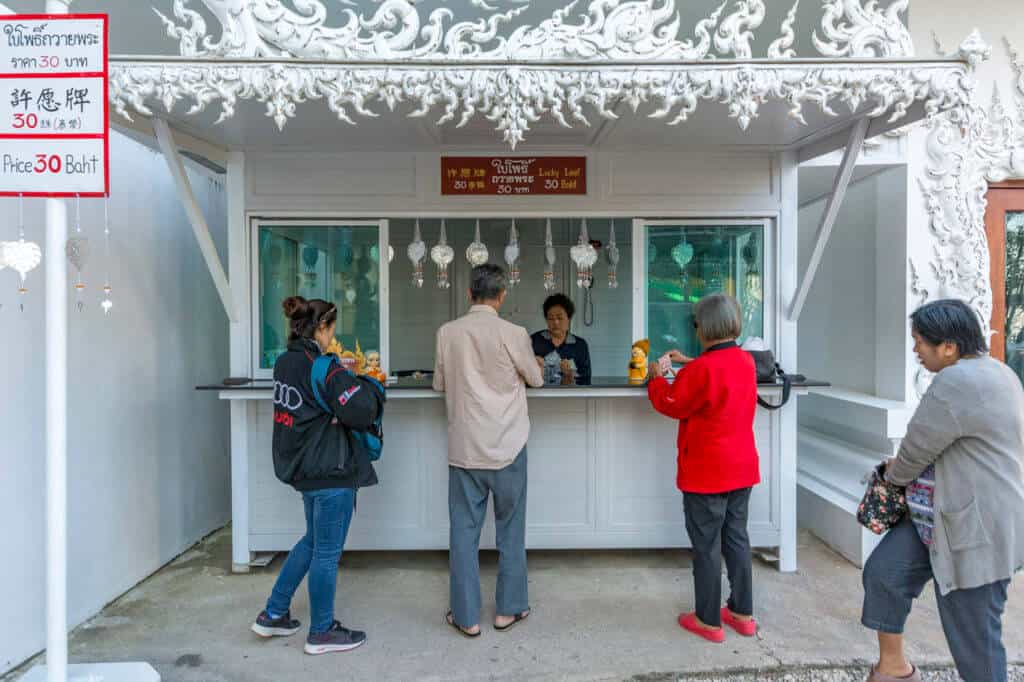 weißer kleiner Verkaufsstand der mit den Einnahmen zum Erhalt und Ausbau des Tempels - Wat Rong Khun beiträgt mit kaufwilligen Touristen